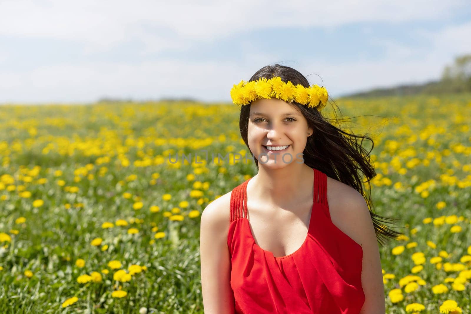 Laughing young girl posing in a dandelion meadow with a wreath of dandelions on her head.