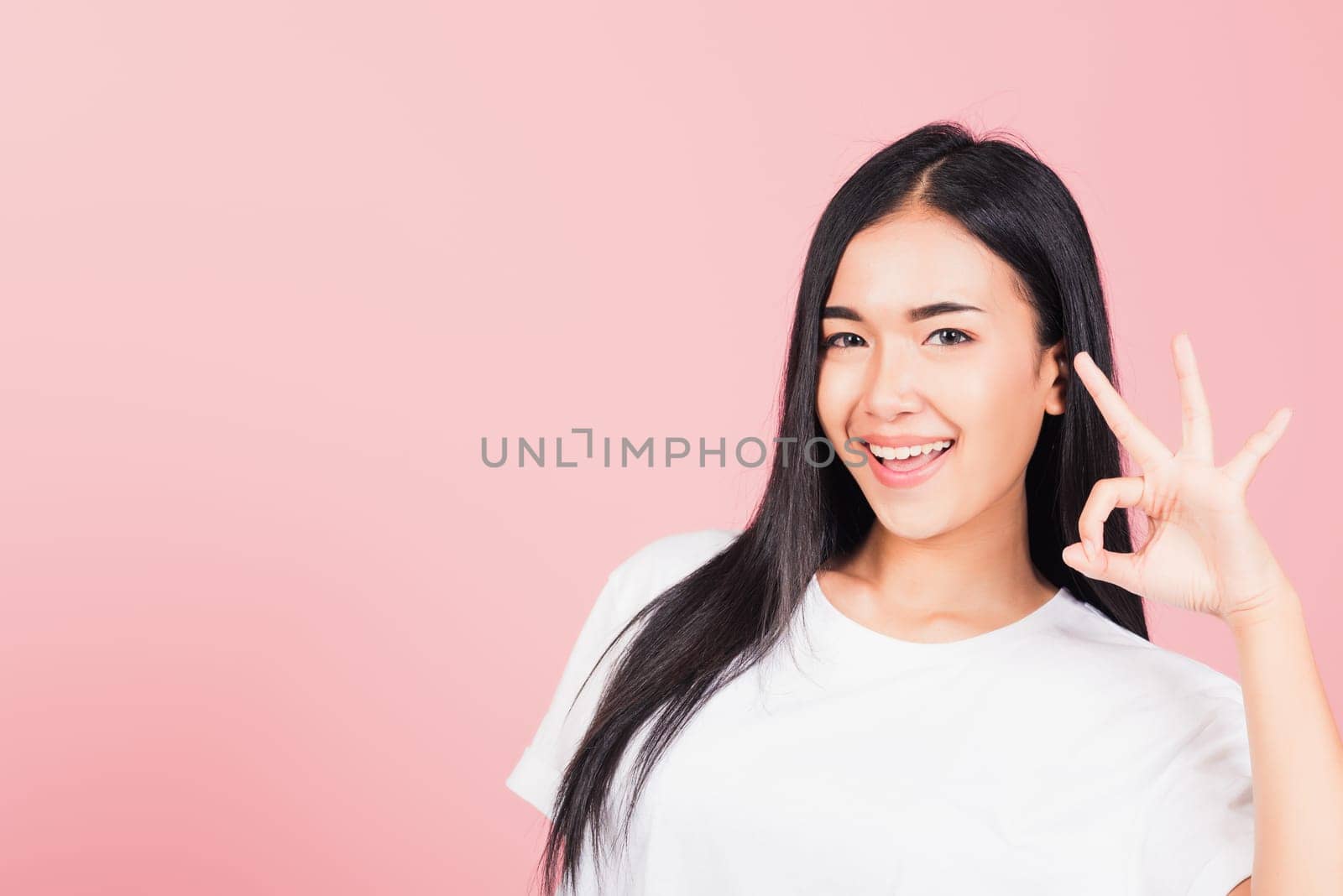 Portrait Asian beautiful young woman standing, She made finger OK symbol sign to agree side away looking at camera, studio shot isolated on pink background, Thai female agree hand sign copy space