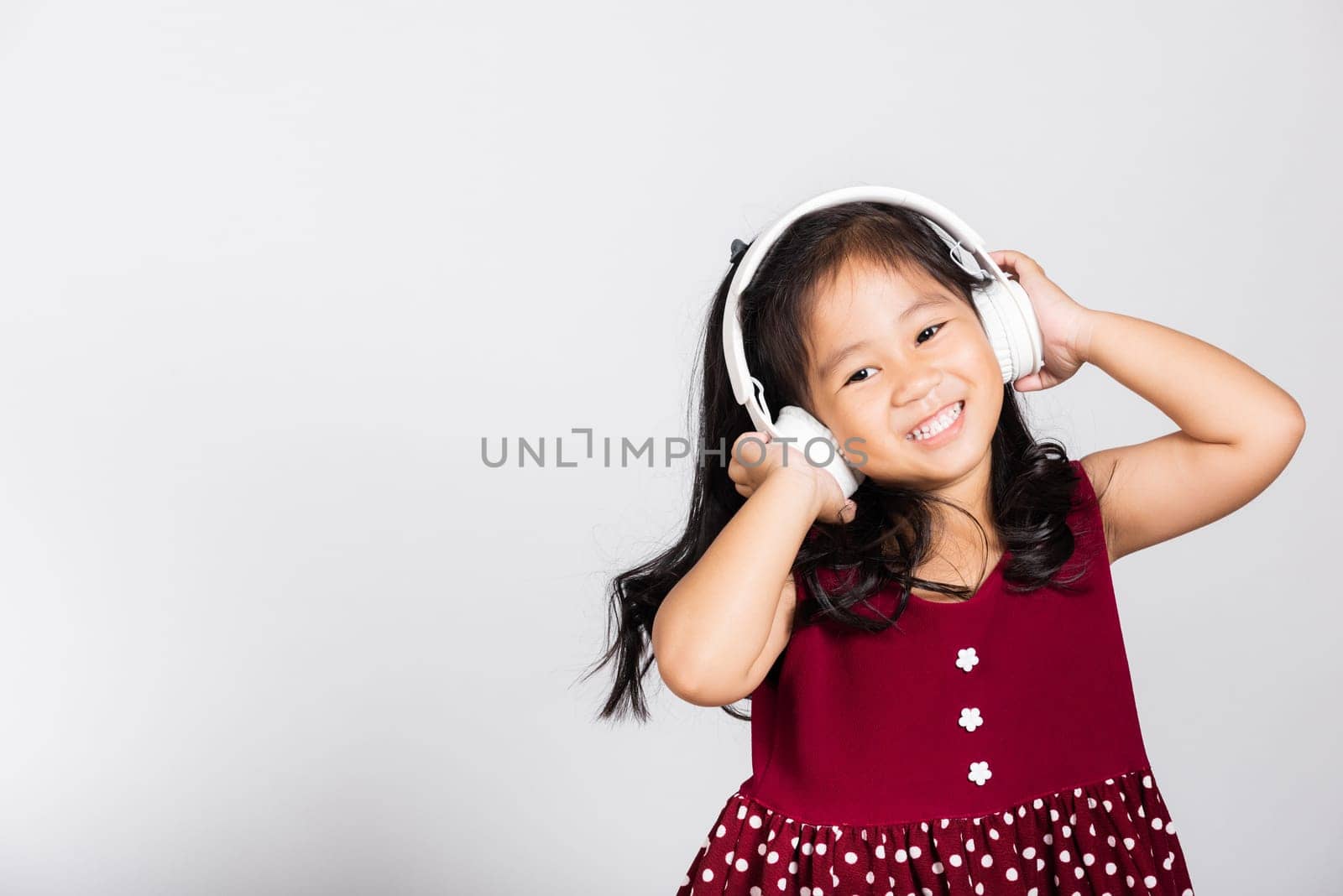 Little cute kid girl 3-4 years old listen music in wireless headphones in studio shot isolated on white background, happy Asian children smiling listening audio, entertainment lifestyle