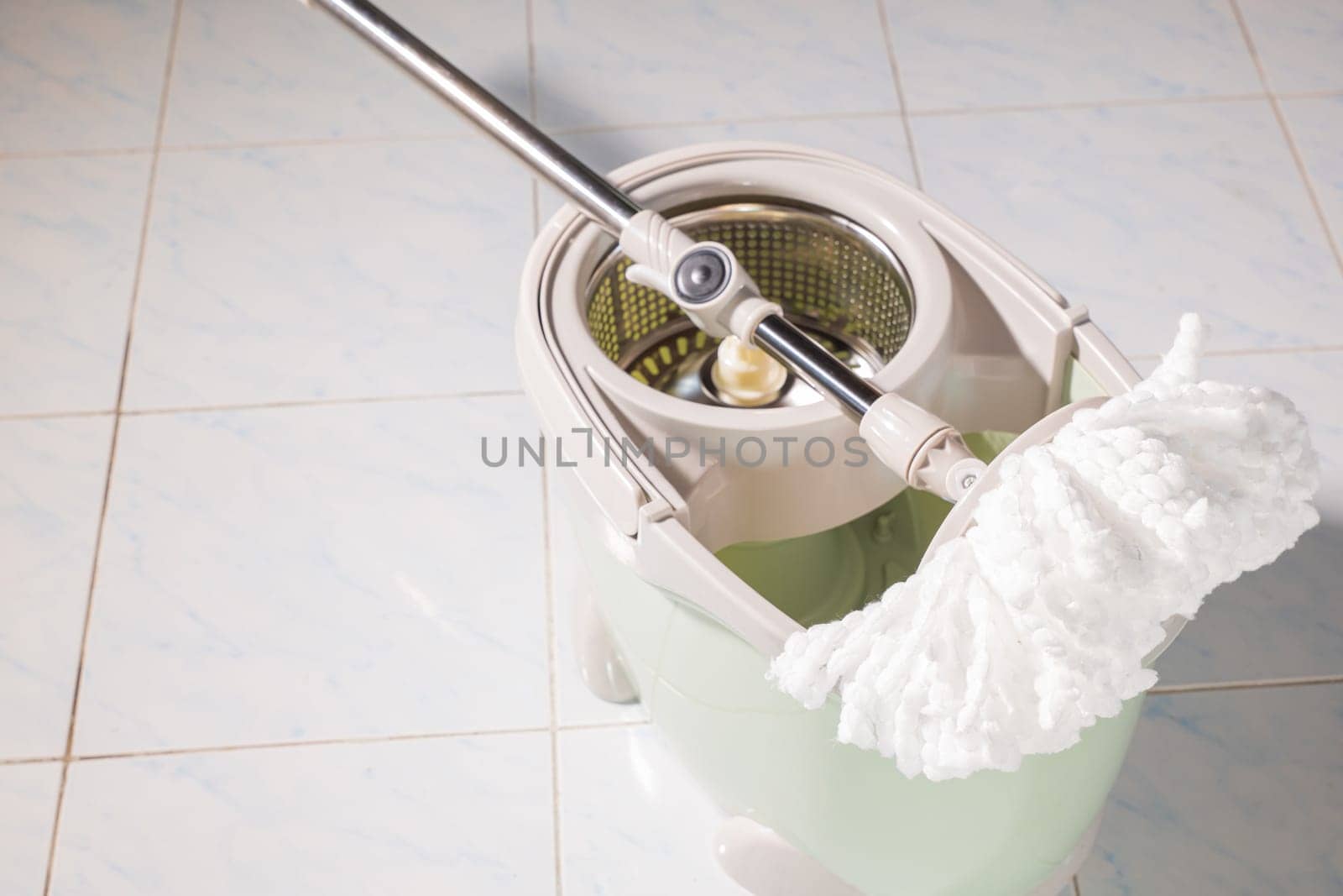 Mop with microfiber head spinning on the bucket next to floor cleaning liquid and mopping the floor house in the living room