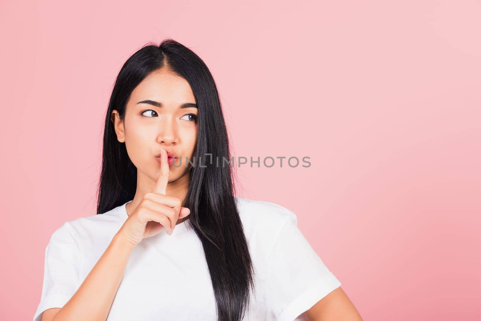 Asian happy portrait beautiful cute young woman smile stand making finger on lips mouth silent quiet gesture studio shot isolated on pink background, Thai female looking to side away with copy space