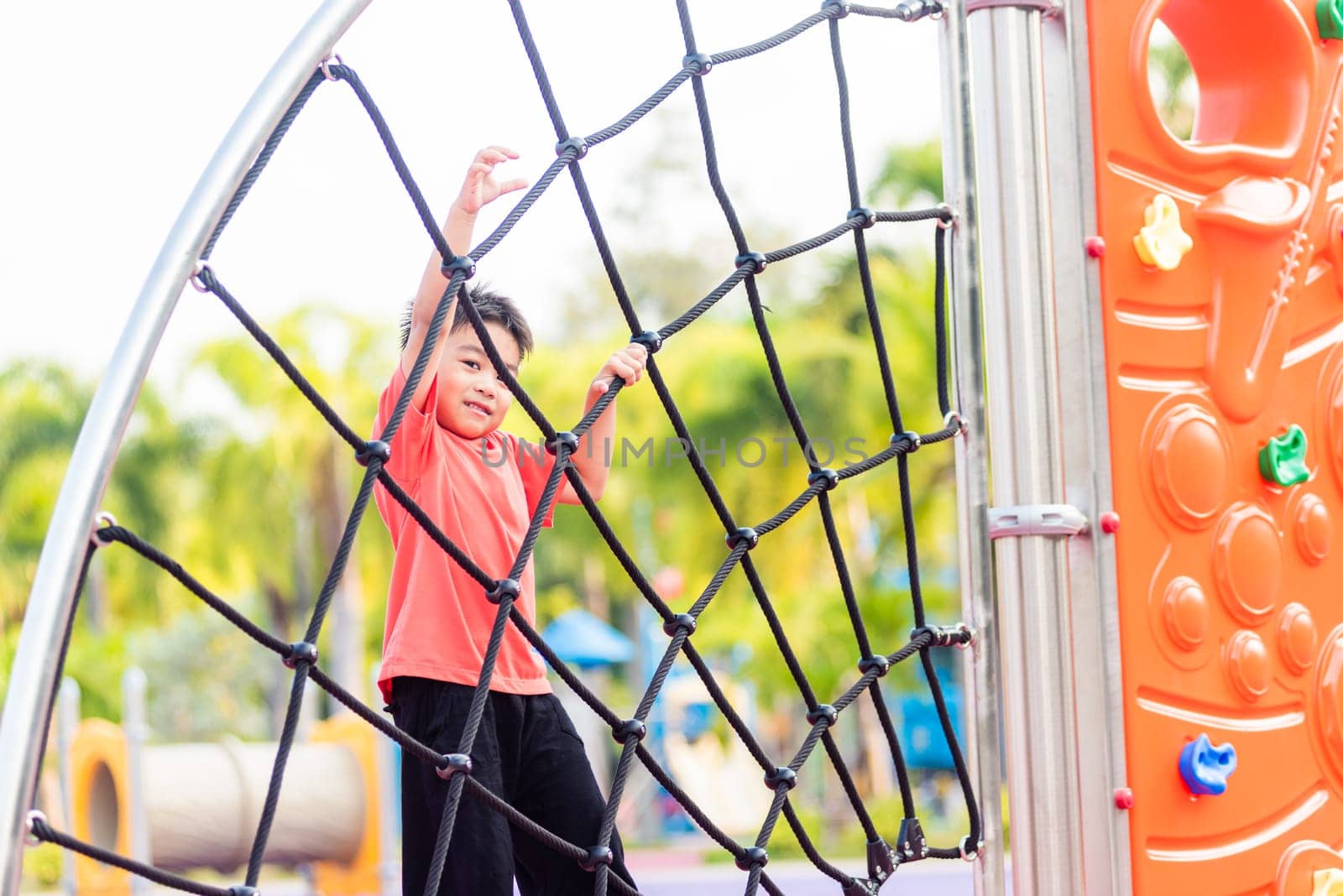 Asian child smiling playing climbing outdoor playground, happy preschool little kid having funny while playing climbs on a rope climbing net on playground equipment in daytime in summer, Little boy