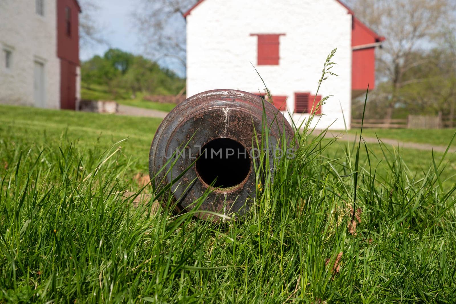 A cannon in the grass at a colonial American iron forge and surrounding village. Closeup look down the barrel, whitewashed buildings in the background of this historic site. Copy space, no people, shot in natural light