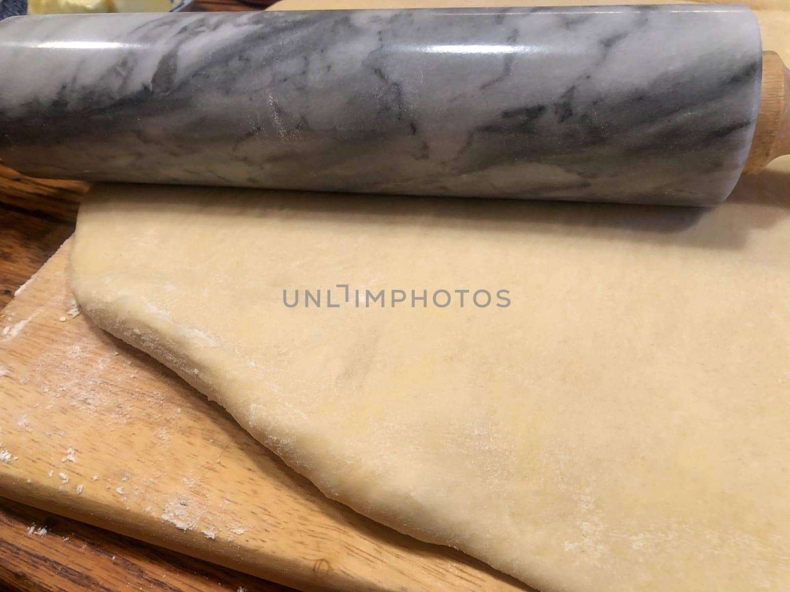 Closeup of traditional rustic kitchen bakery wooden countertop, and cutting board with tender dough rolled out and swirled granite rolling pin. Warm cozy lighting for artesanal feel, no people, with copy space
