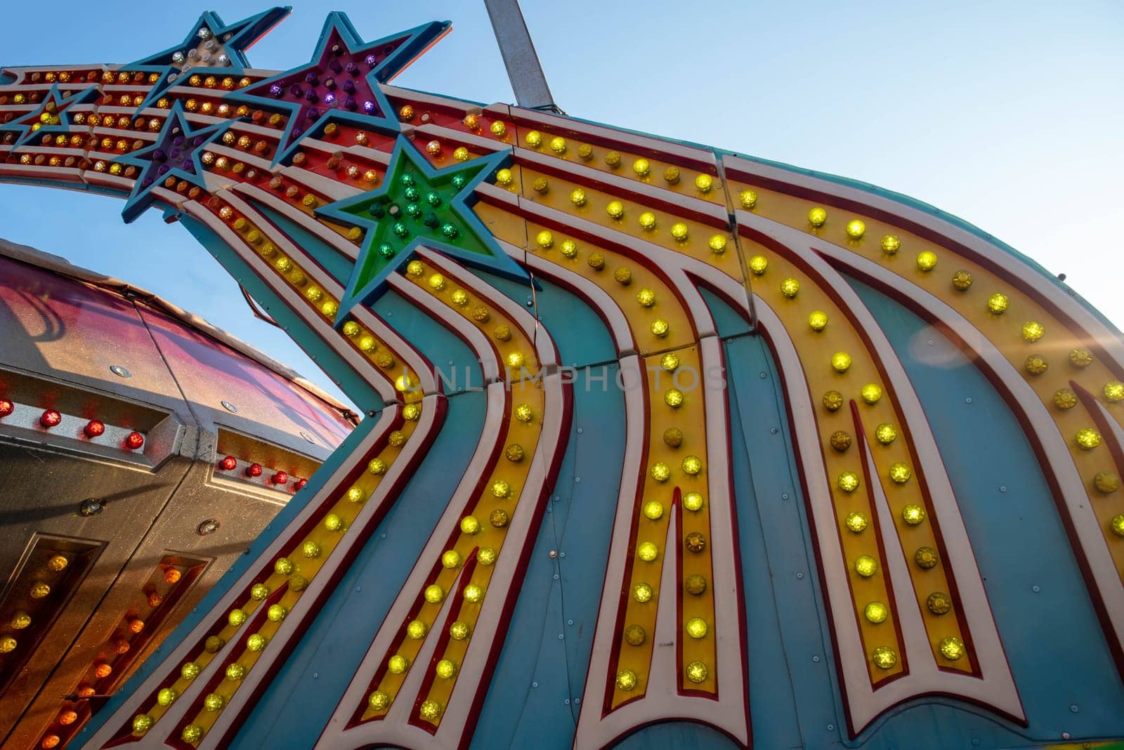 bold bright colorful light bulbs on amusement park ride shaped like shooting stars shot outdoors in natural light blue sky background with copy space