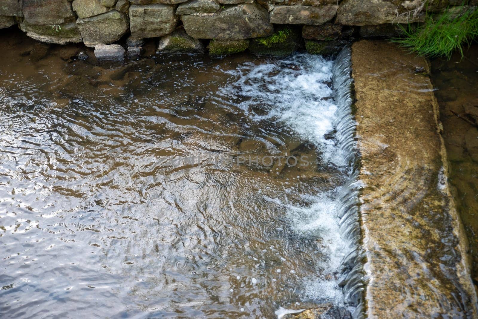 Stone lined man made channel of flowing water cascades over an old colonial American Pennsylvania dam with texture water ripples and copy space in natural light with no people.