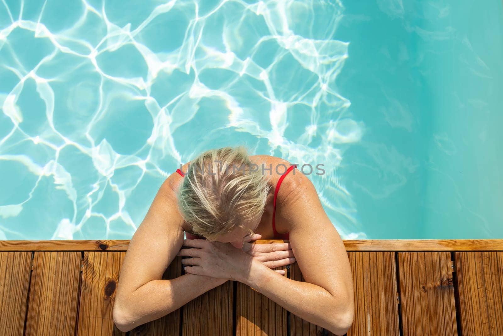 Top view of woman standing in swimming pool and leaning on wooden edge.