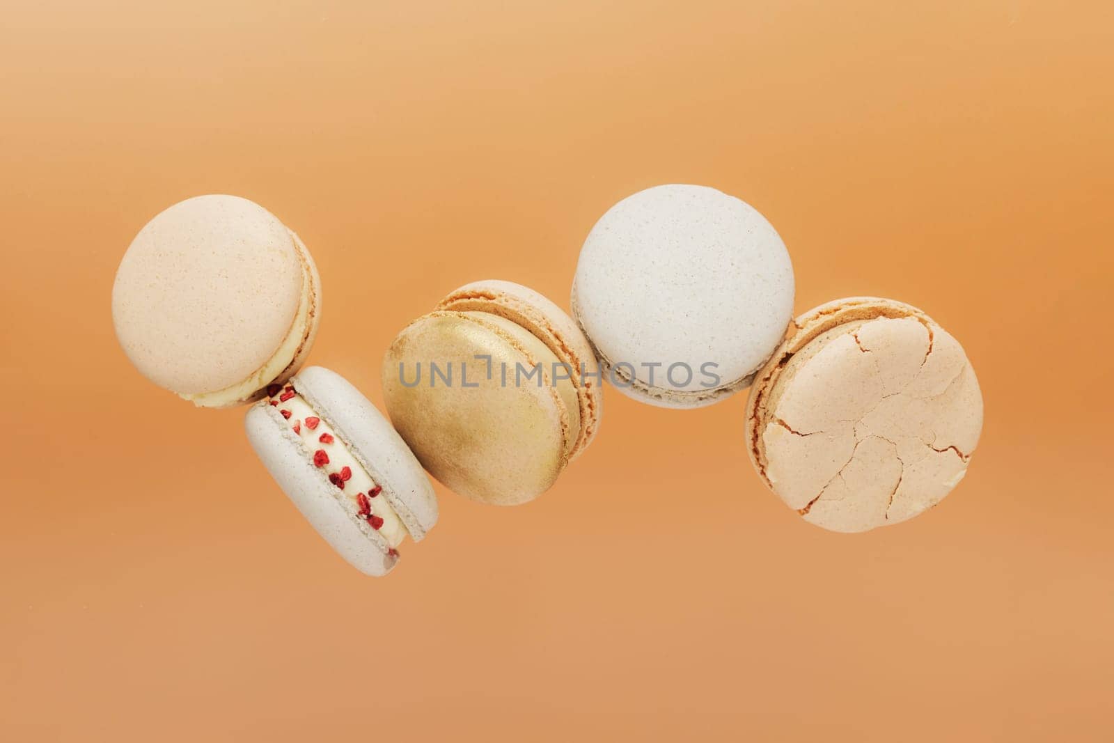 White, yellow, gold macaron cookies flying, falling in motion or levitating. Colorful, sweet small French macaroon cakes. Light yellow background. Broken cut, bitten parts, halves. High quality photo