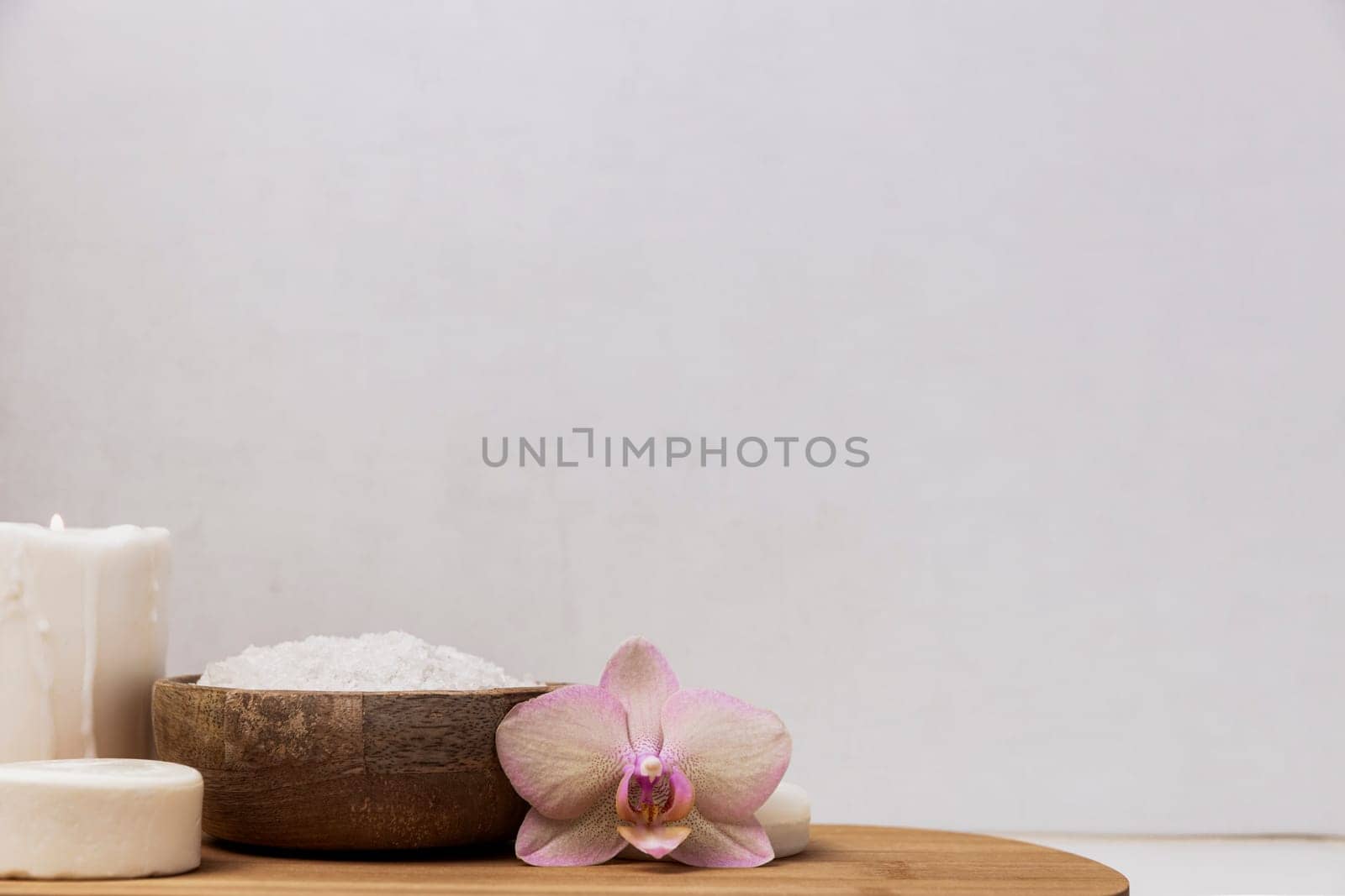 Preparation for hotel spa treatment, home bath procedure. Gray washbasin in bathroom, accessories on wooden tray. Burning candle, sea salt in bamboo bowl, orchid flower, homemade eco soap