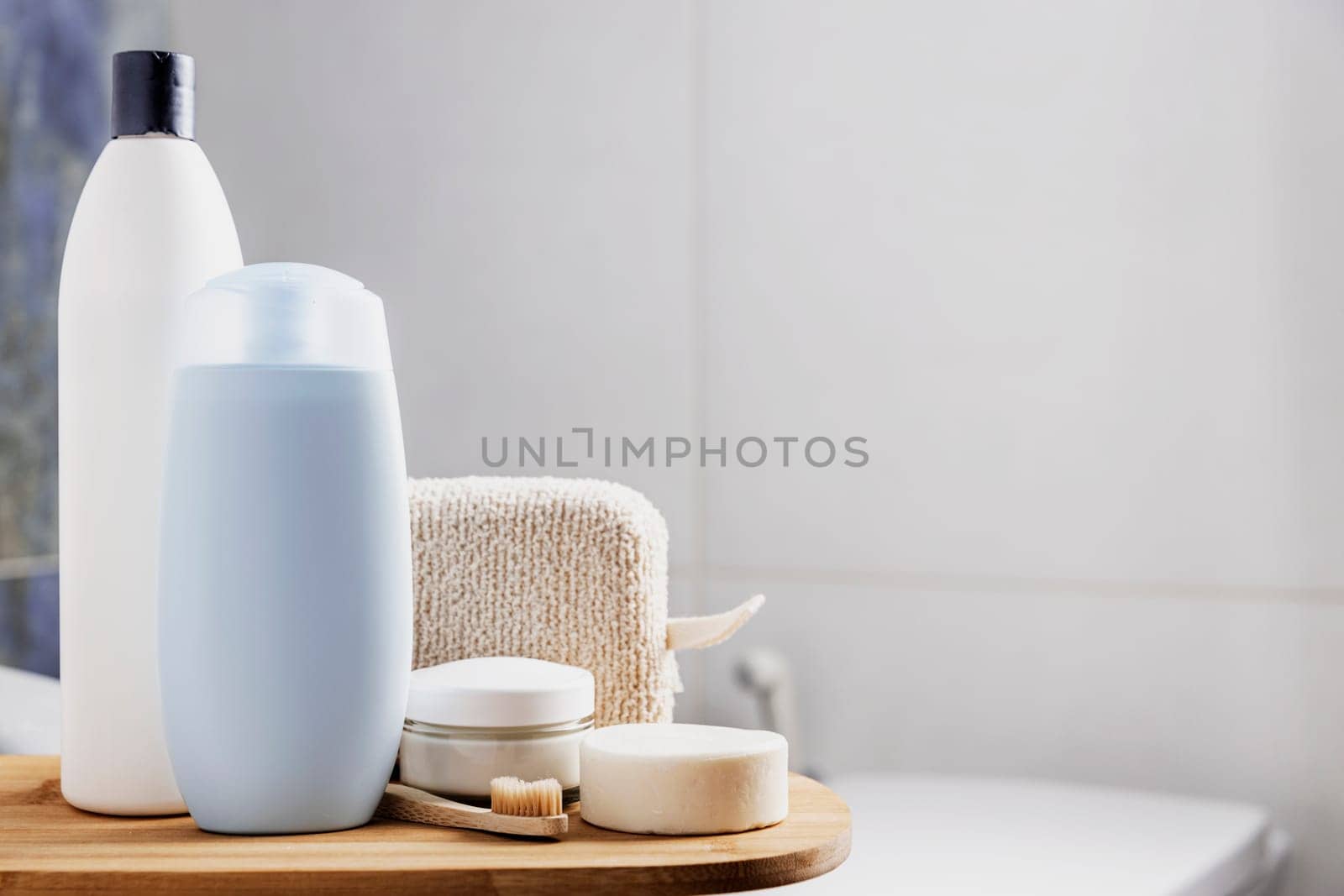 Preparation for hotel spa treatment or home bath procedure. Gray bathroom with accessory and cosmetics on tray on washbasin table. Shampoo, shower gel, washcloth, soap, tooth brush, cream, white soap