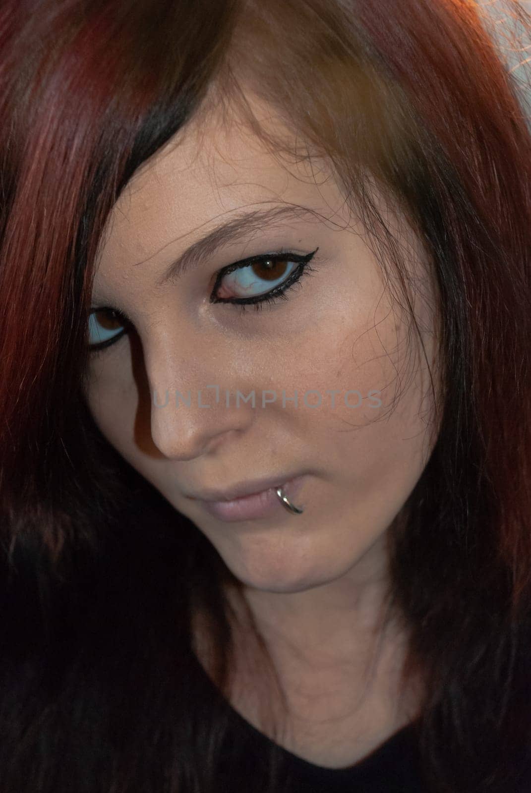 Young punk emo Girl with piercing, with red and black hair, looking at camera with serious facial expression, close-up