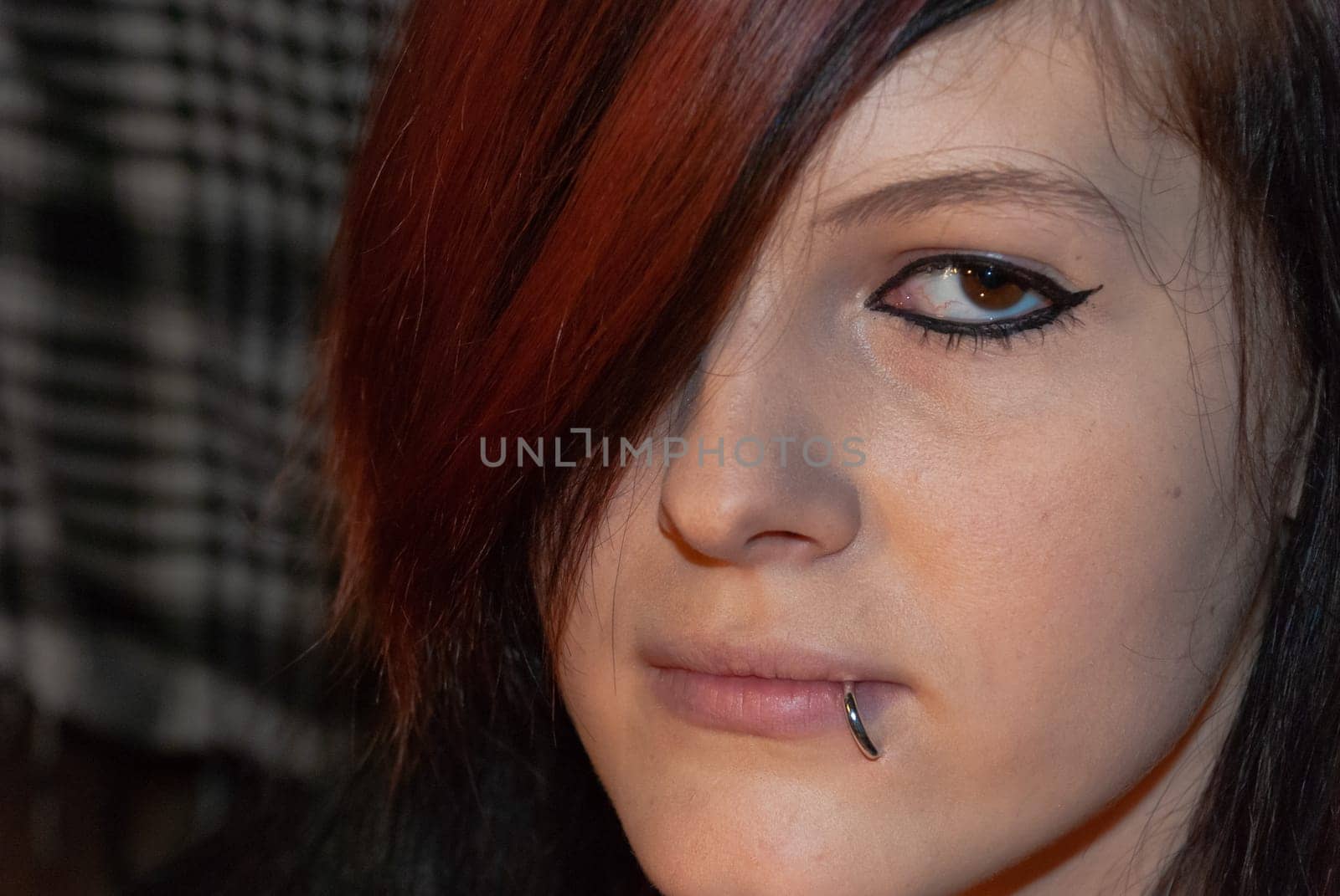 Young punk emo Girl with piercing, with red and black hair, looking at camera with serious facial expression, close-up
