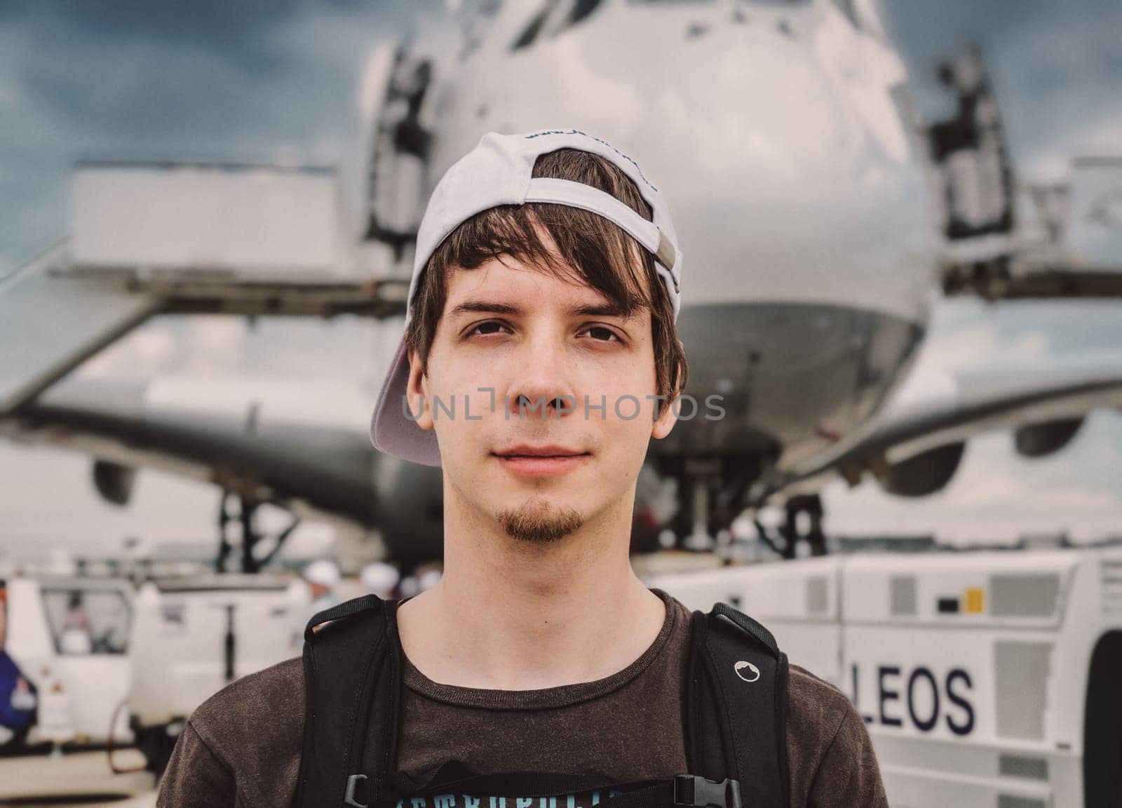 Young adult man passenger looking at camera while standing in front of a big airplane at the airport
