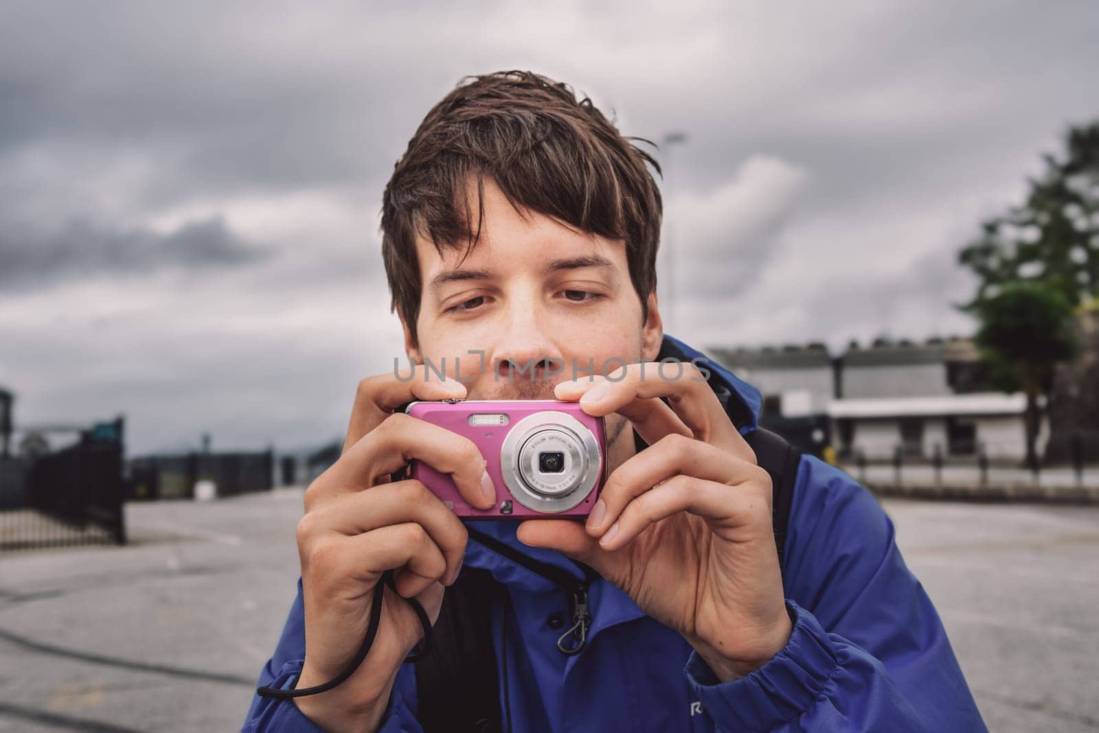 Young adult man with brown hair taking a photo with a retro old pink digital camera