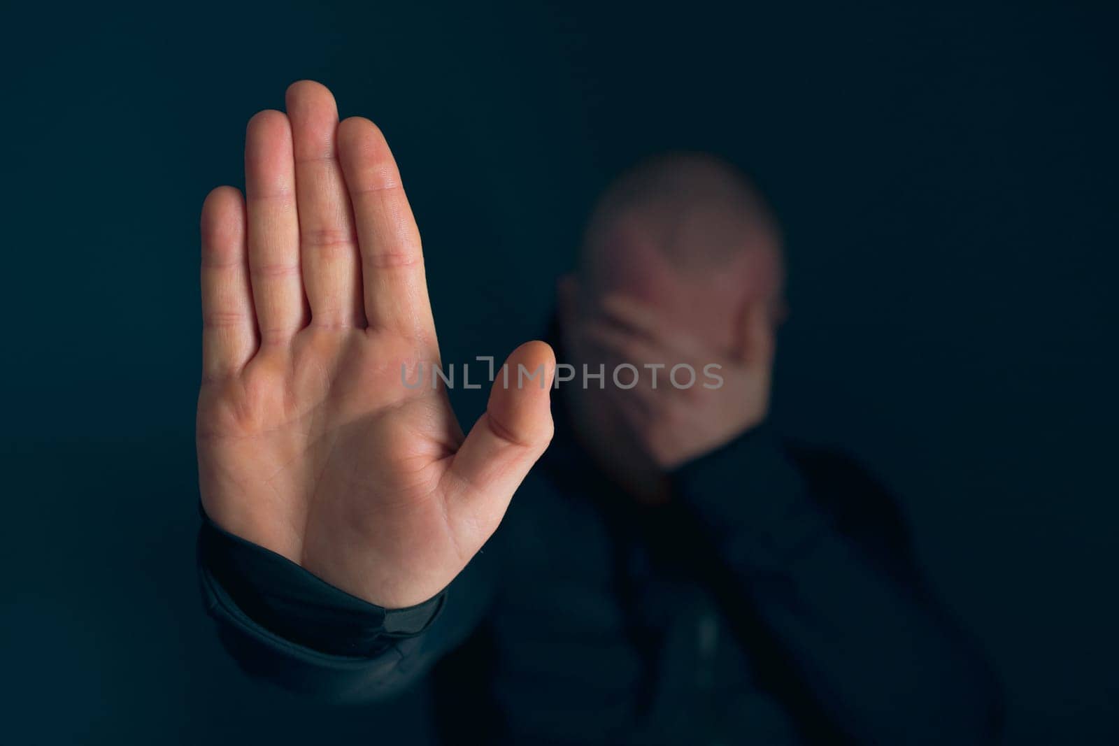 Sad, angry man showing stop sign on dark background. Low key photo.