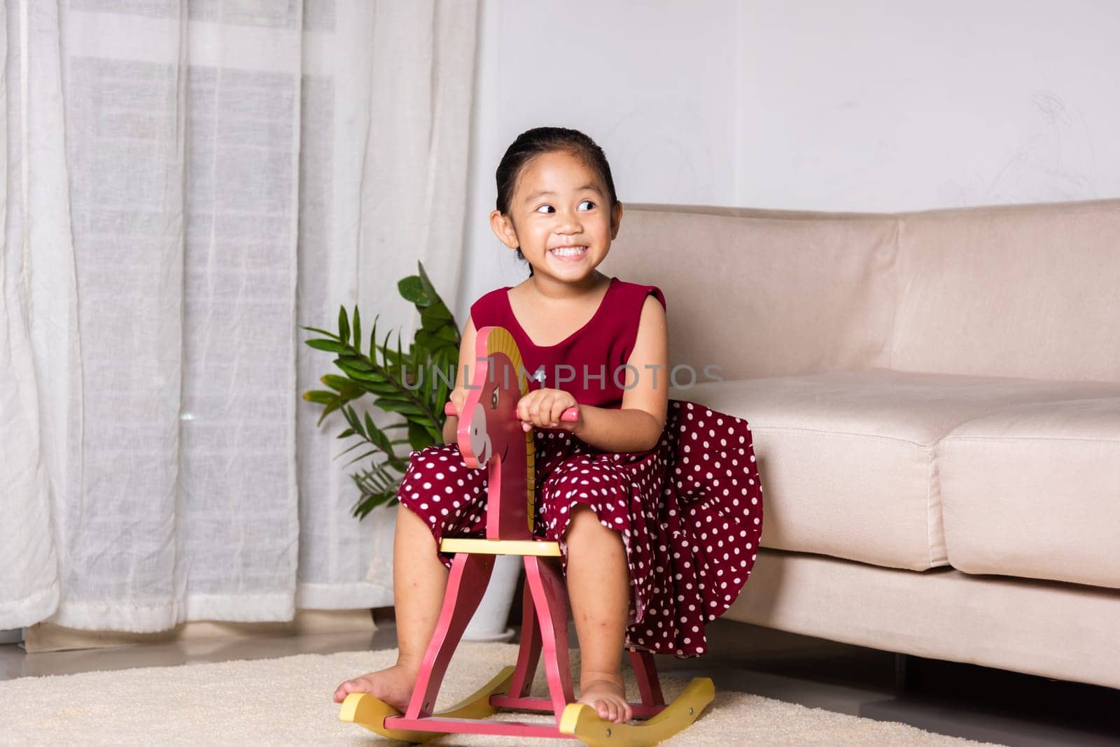 Asian cute little girl swinging riding toy horse, Smiling kid playing horse rocking chair at home in living room, Happy time to play during self kindergarten preschool