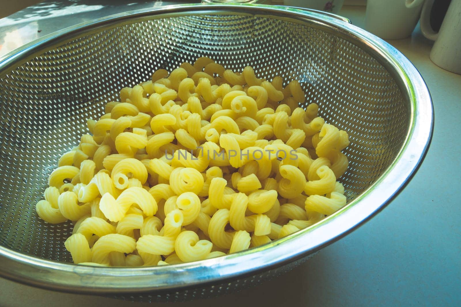 Yellow pasta in an aluminum colander on the white table