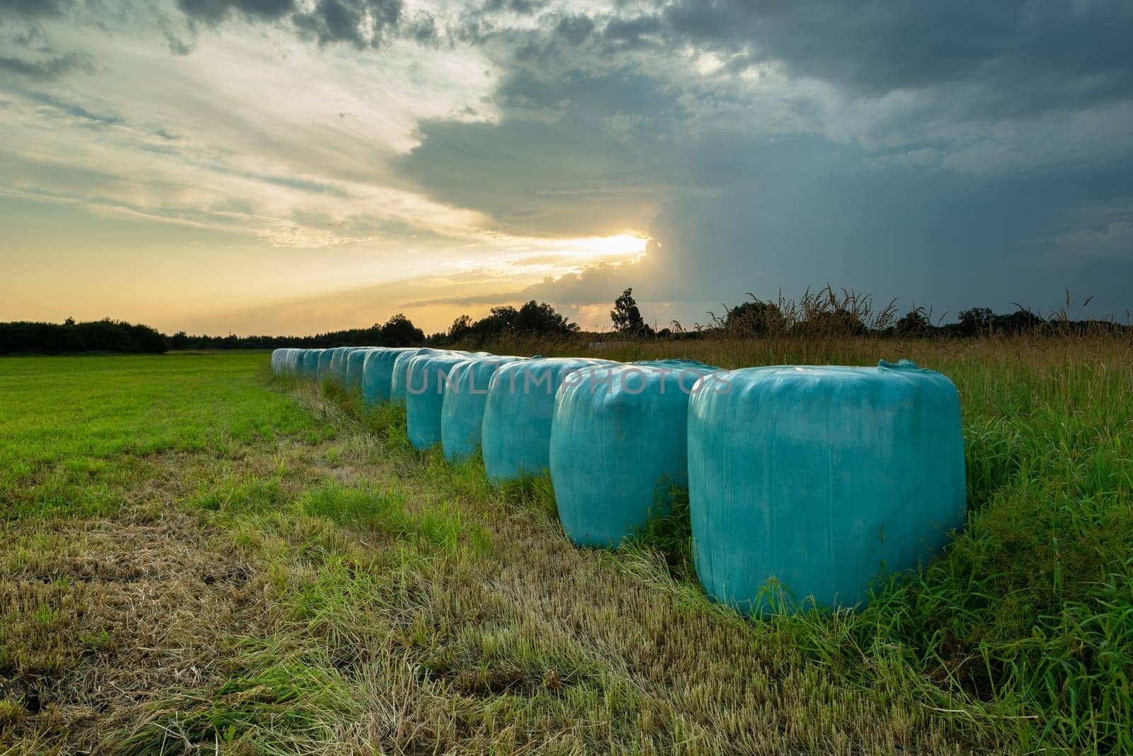 Hay bales in foil and the sunset behind the clouds, Nowiny, Poland