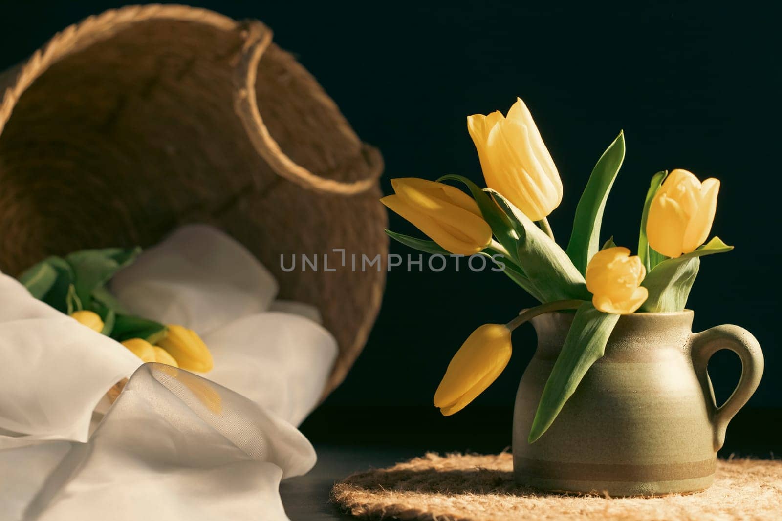 Still life with bouquet of yellow tulip flowers in old vintage jug, in beam of light on dark background.Art photography.