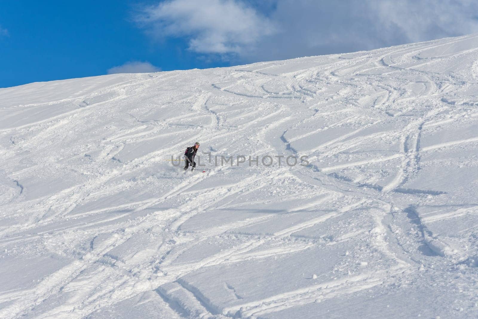 Woman with brown hair, wearing ski wear and a bagpack skiing down a beautiful snow hill with plenty of tracks on the snow, view from the side from far away, stryn norway, horizontal