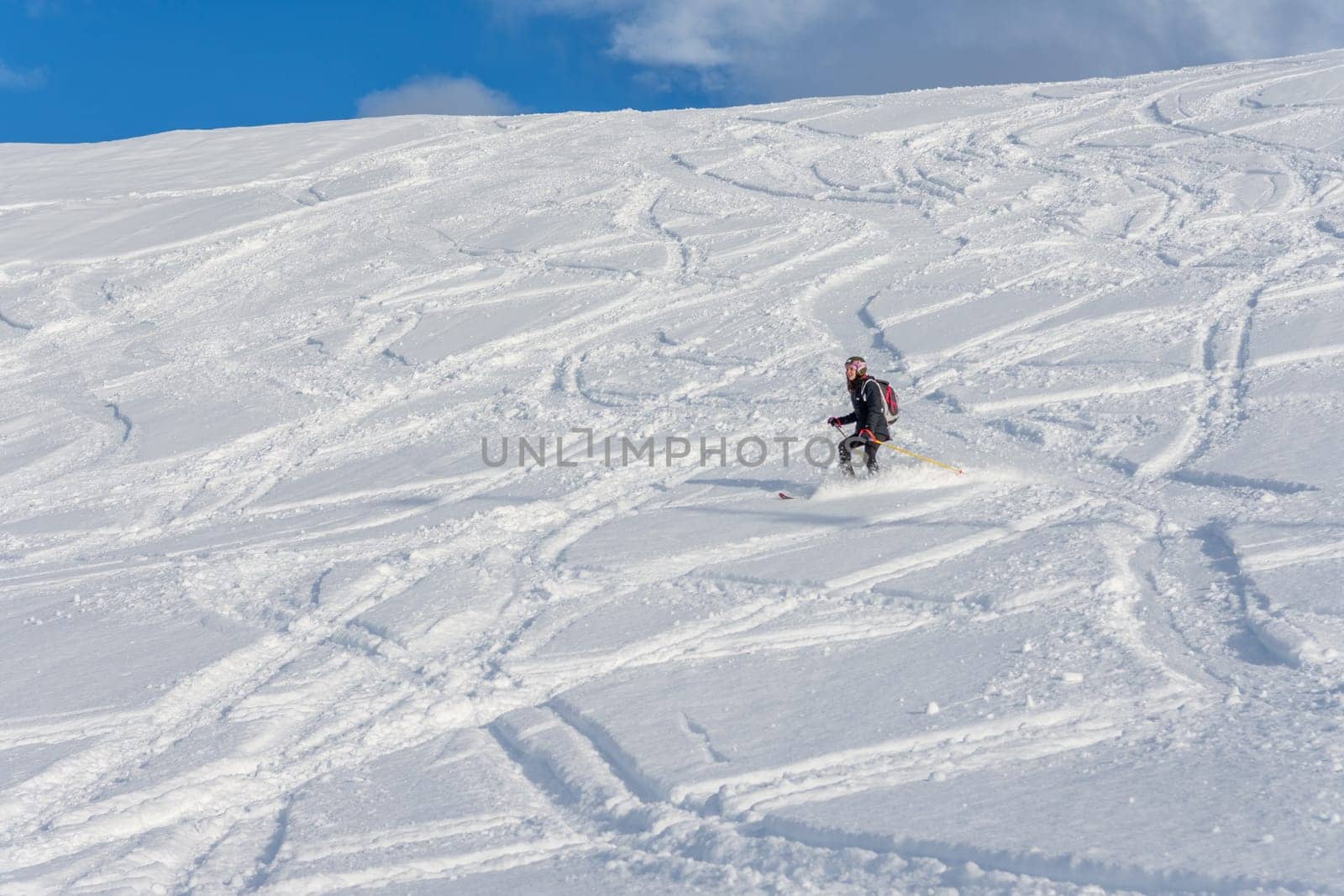 Woman with brown hair, wearing ski wear and a bagpack skiing down a beautiful snow hill with plenty of tracks on the snow, view from the side from far away, stryn norway, horizontal