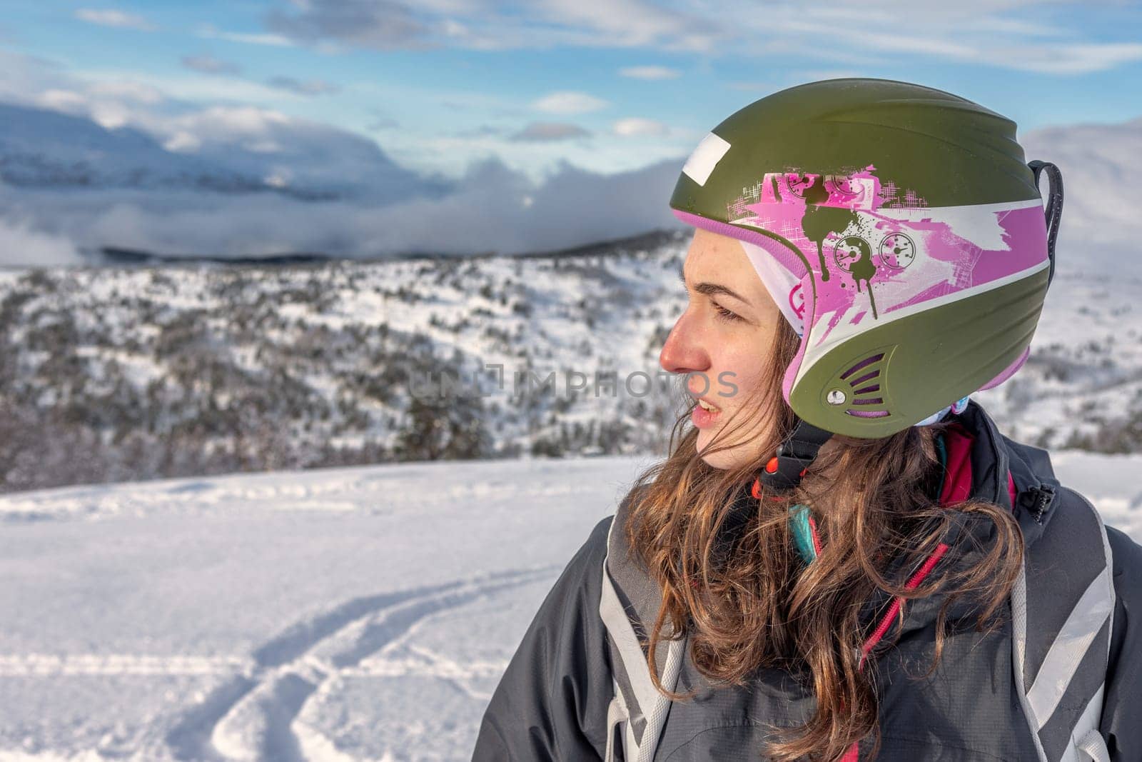 Women with brown standing on top of a mountain, wearing ski helmet and ski wear, serious facial expression, looking at ski slope, stryn norway, horizontal