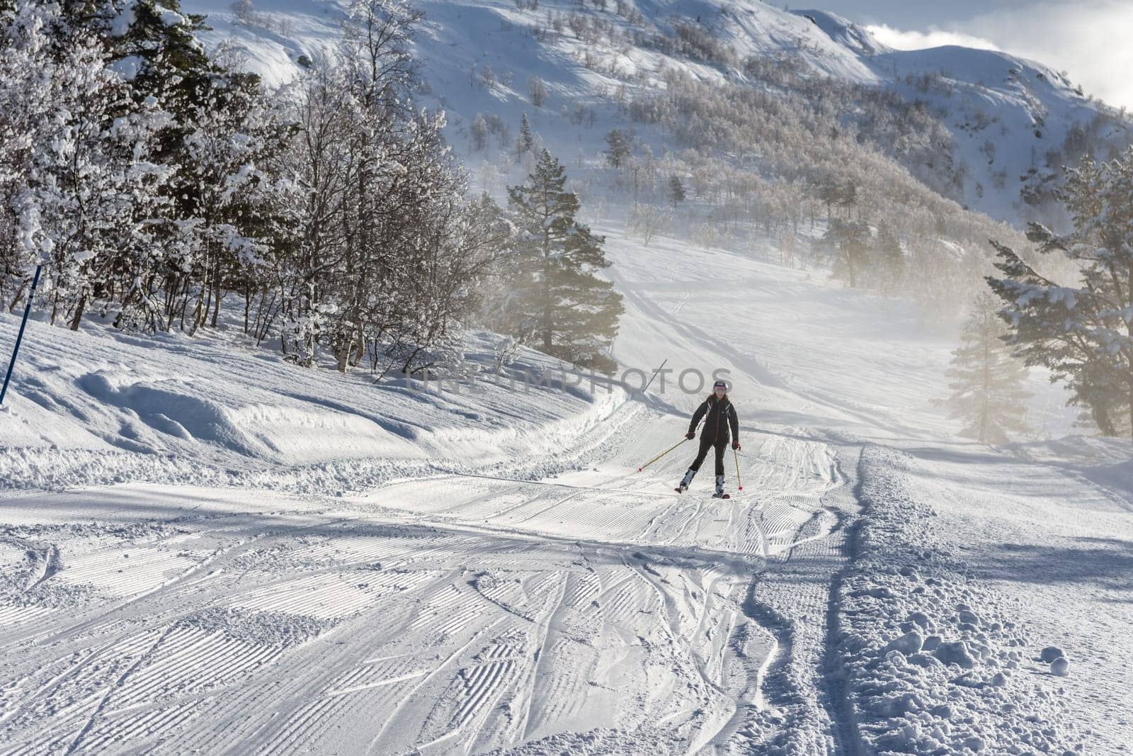 Woman with brown hair smiling, wearing ski wear and a backpack skiing down a track from top of the mountain in ski centre stryn, norway, view from distance, horizontal