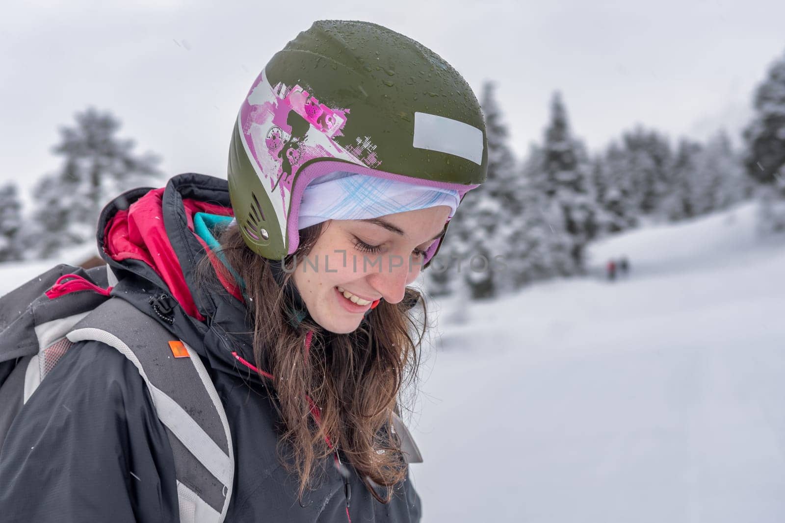 Woman with brown hair wearing ski wear and ski helmet looking down with eyes closed, smiling cheerful, side view, stryn norway, close-up, horizontal