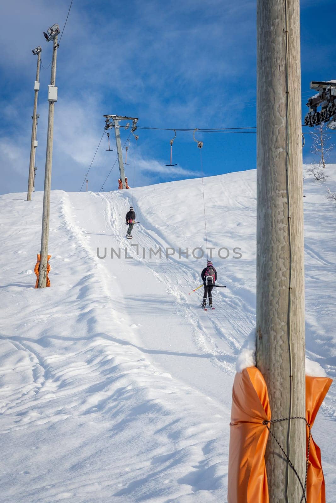 Woman with ski and man with snowboard wearing black sports clothes, using ski lift, moving up to the top of the mountain, rear view, vertical