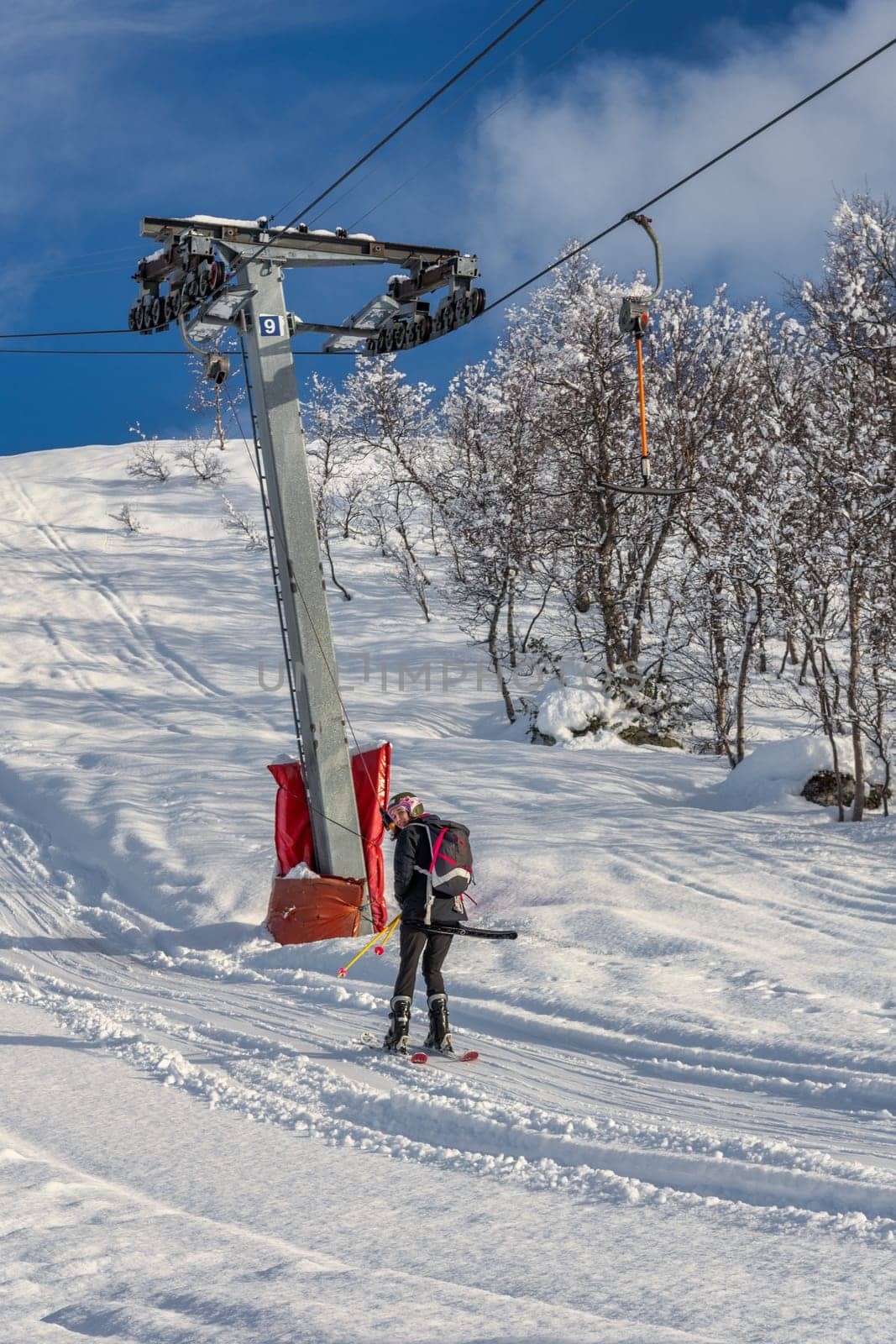 Skiing Woman with brown hair and black ski wear, smiling, looking back at camera while using a ski lift, rear view, vertical
