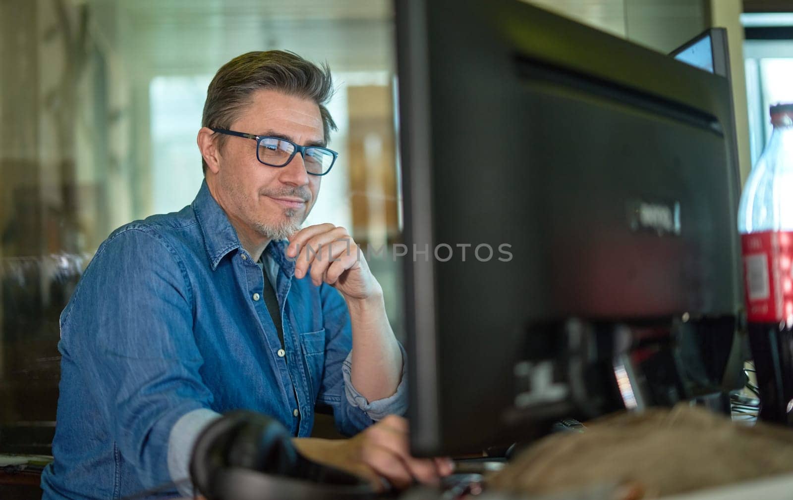 Businessman working with computer in office. Business lifestyle - casual middle aged man sitting at desk in front of screen, smiling, happy.