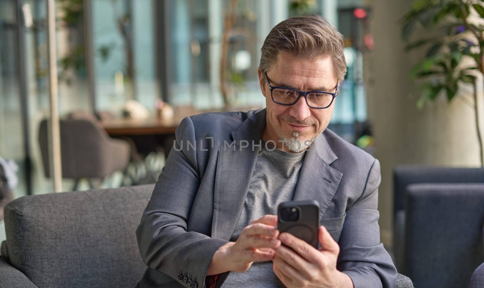 Businessman using phone in office lobby or on cafe terrace. Happy middle aged man, entrepreneur, small business owner working online.