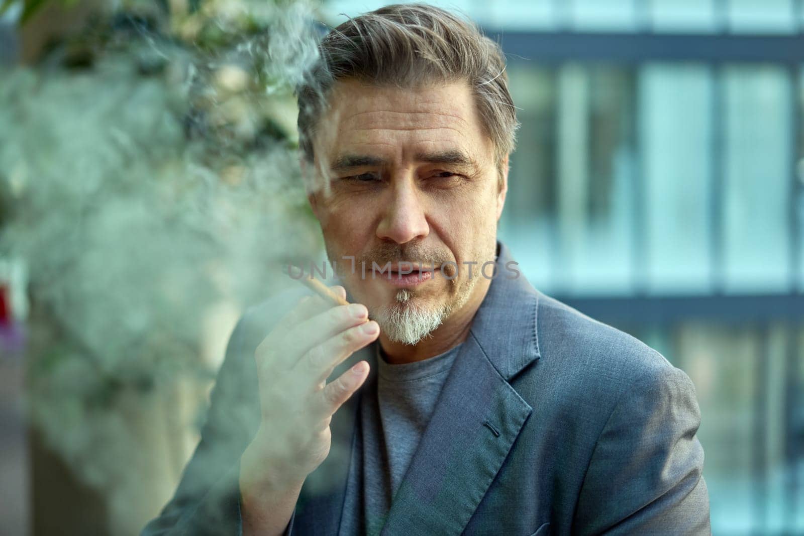 Middle age man smoking cigar outdoor in front of office building, thinking, looking away.