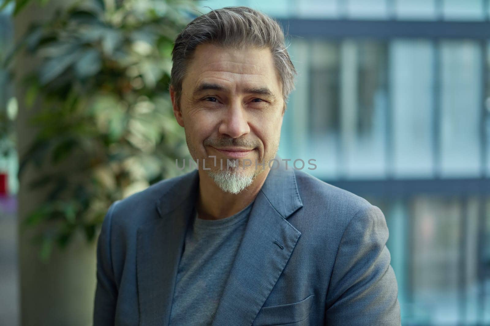 Middle aged confident businessman in business casual in office. Portrait of happy mid adult man in 50s, smiling, looking at camera.