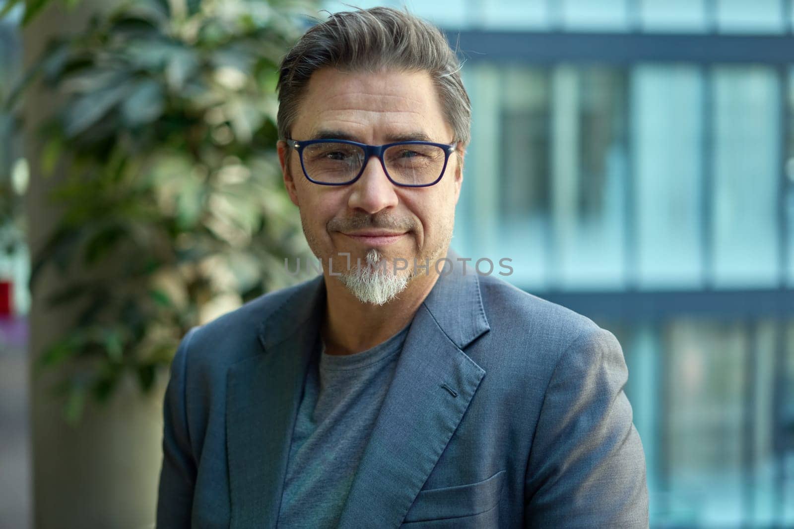 Middle aged confident businessman in business casual in office. Portrait of happy mid adult man in 50s, smiling, looking at camera.