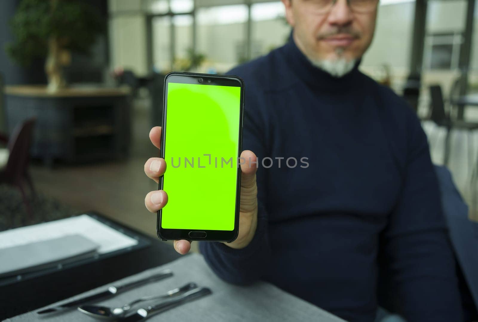 Man sitting in restaurant or cafe using showing phone with blank green screen. Restaurant, food order application.