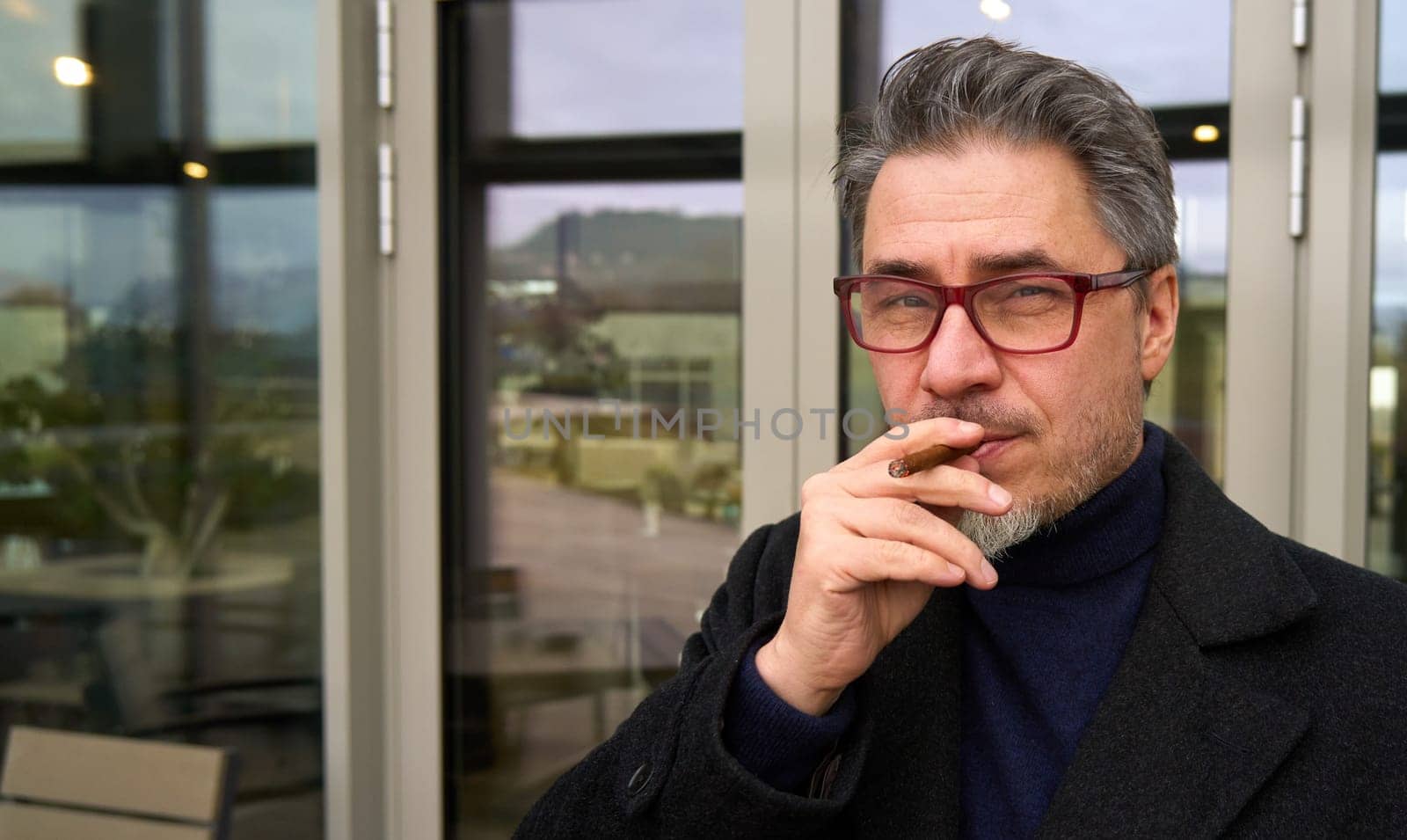 Middle age man smoking cigar outdoor in front of office building.