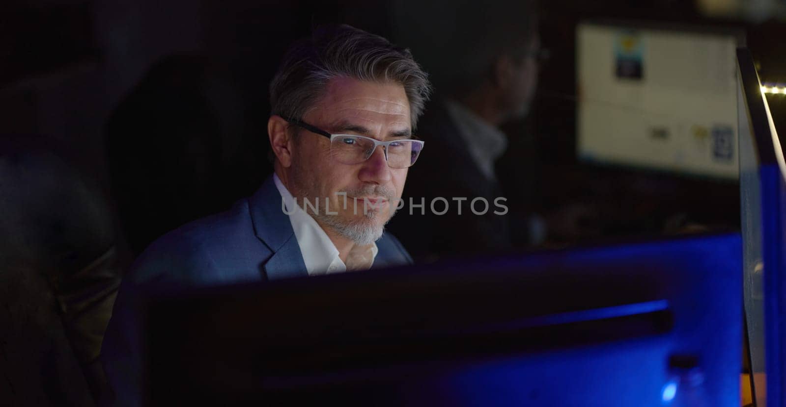 Businessman working with computer at office desk, thinking, smiling. Portrait of happy mid adult man in shirt and jacket, smiling. Bearded, glasses.