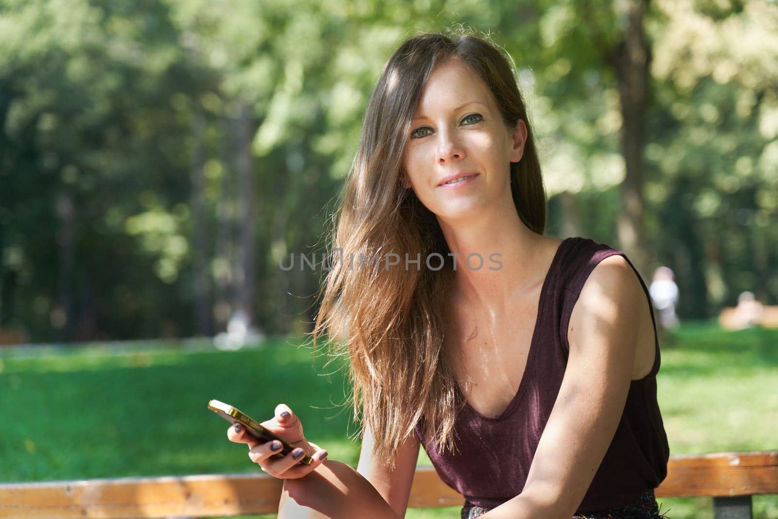Happy young white woman using phone outdoor, smiling.