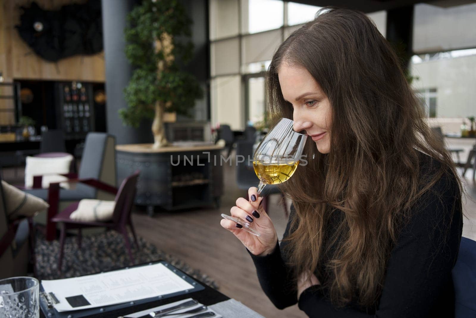 Portrait of woman sitting in restaurant, drinking, smelling, tasting wine, smiling.