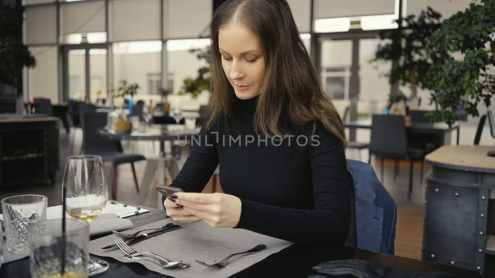Happy smiling middle age woman using phone sitting in restaurant or cafe.