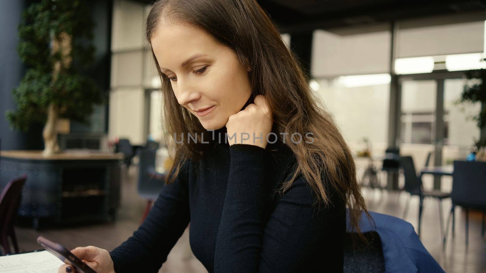 Happy smiling middle age woman using phone sitting in restaurant or cafe.