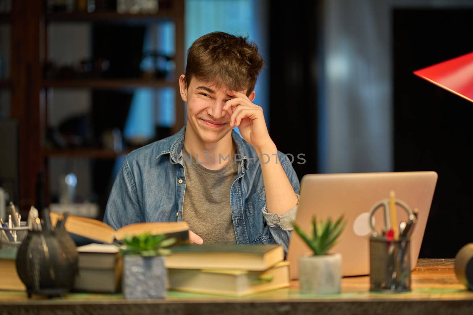 Teenage student learning at home with books and laptop computer. Online school and education, sitting at desk.
