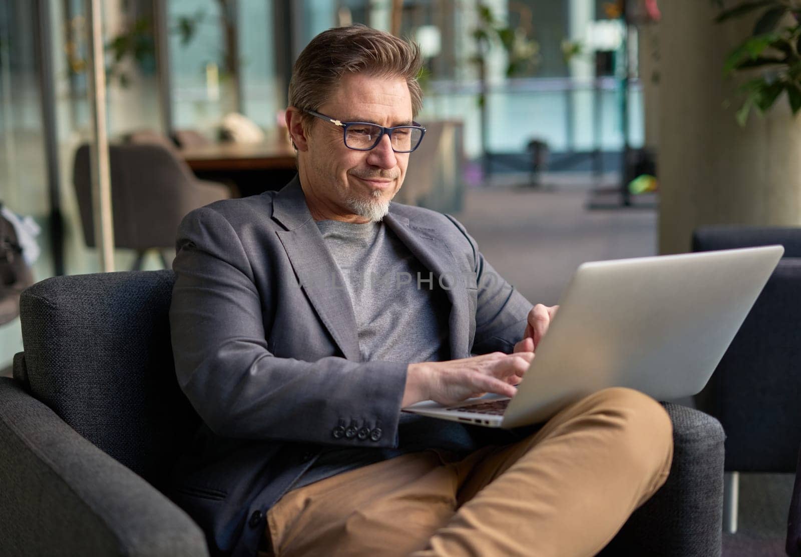 Businessman using laptop computer in office lobby or on cafe terrace. Happy middle aged man, entrepreneur, small business owner working online.
