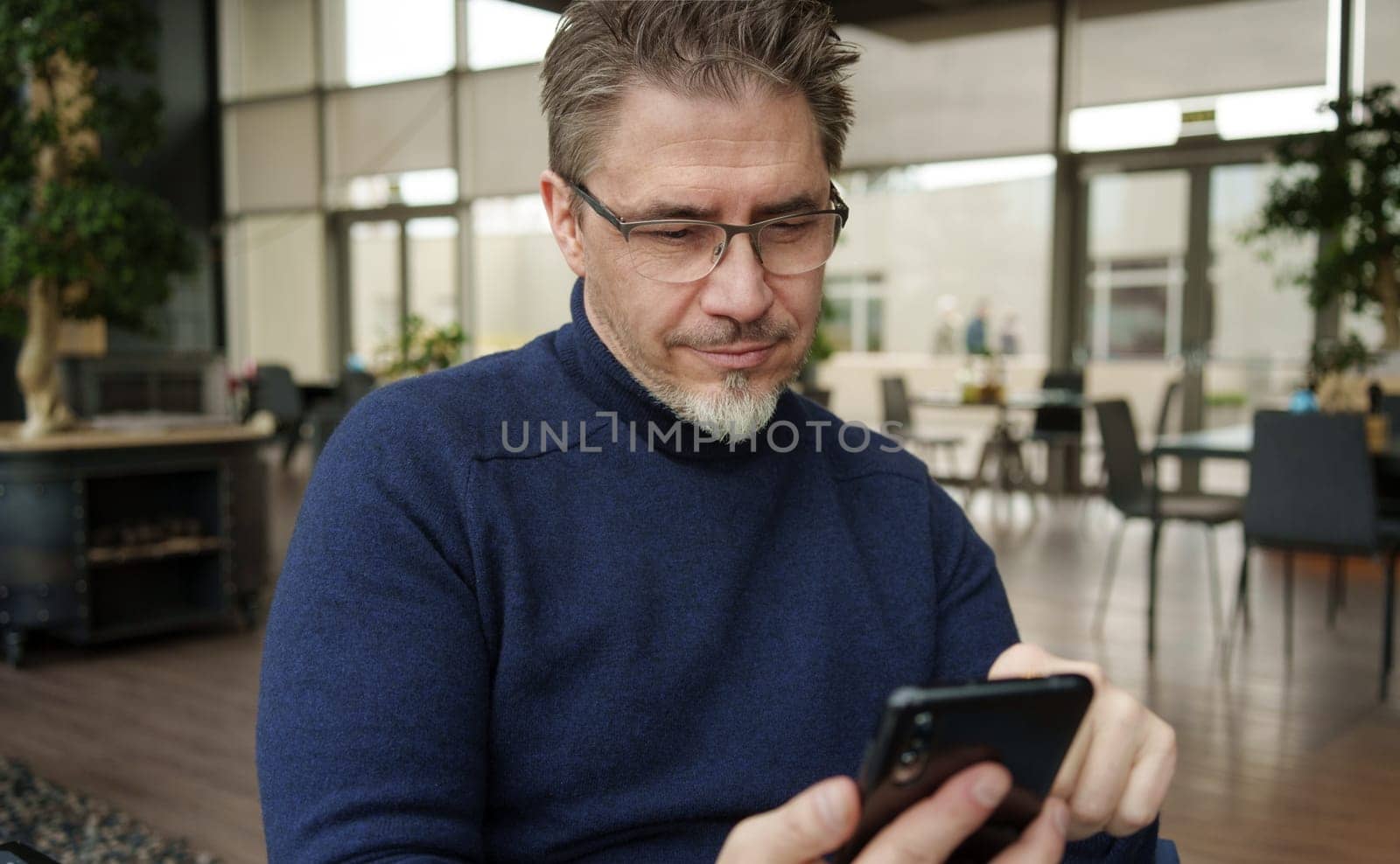 Smiling middle age man using phone sitting in restaurant or cafe.