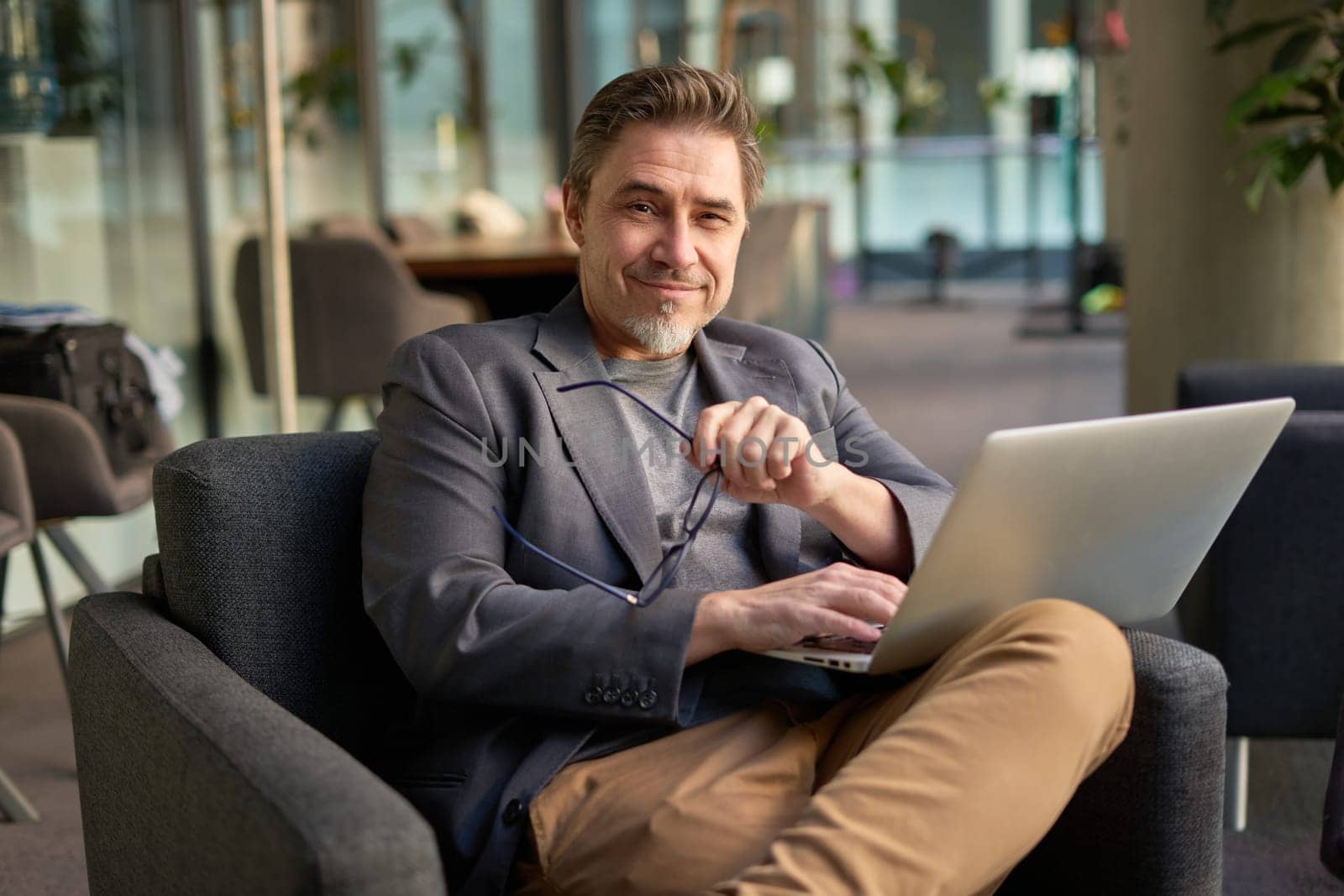 Businessman using laptop computer in office lobby or on cafe terrace. Happy middle aged man, entrepreneur, small business owner working online.