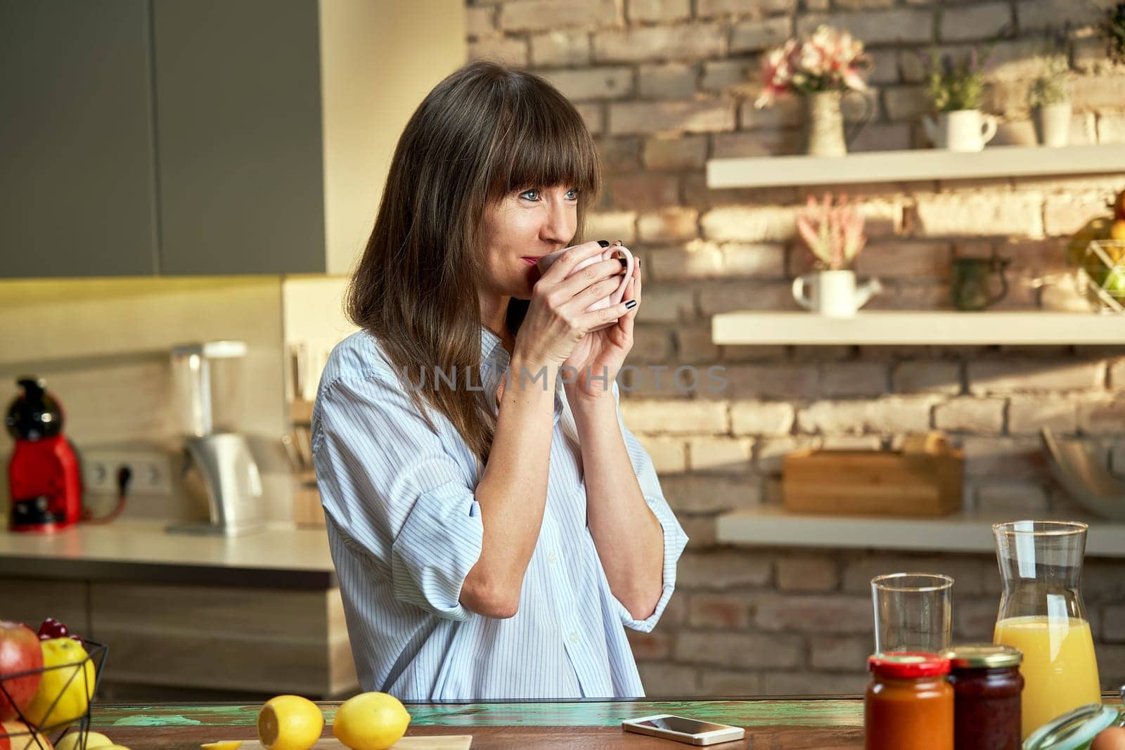 Happy white woman at home drinking coffee at morning in kitchen.