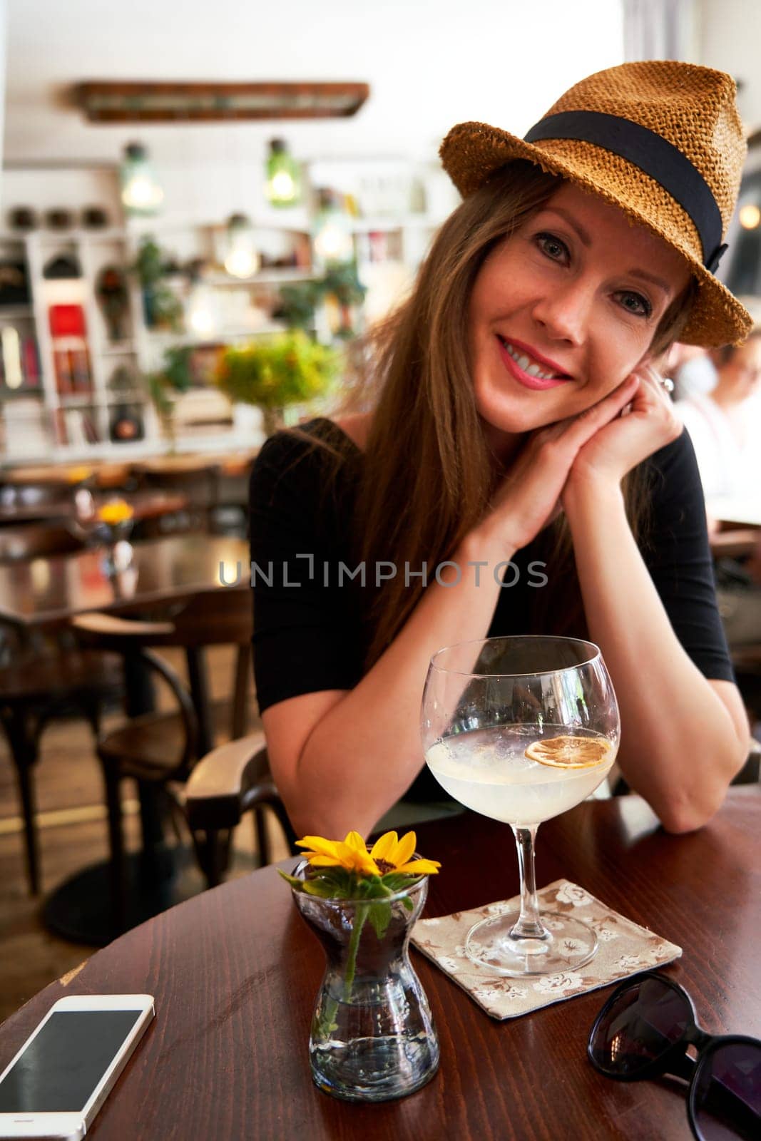 Young happy cute white woman in hat drinking gin tonic cocktail in cafe restaurant