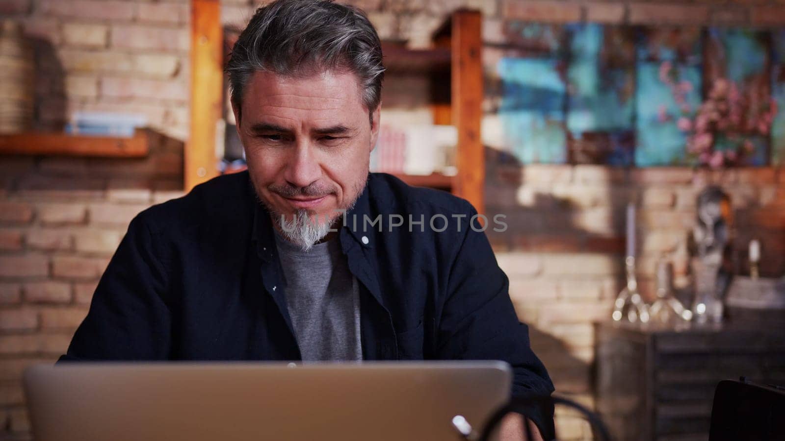 Mature adult man in 50s working on laptop in home office, working from home online, using internet, thinking.