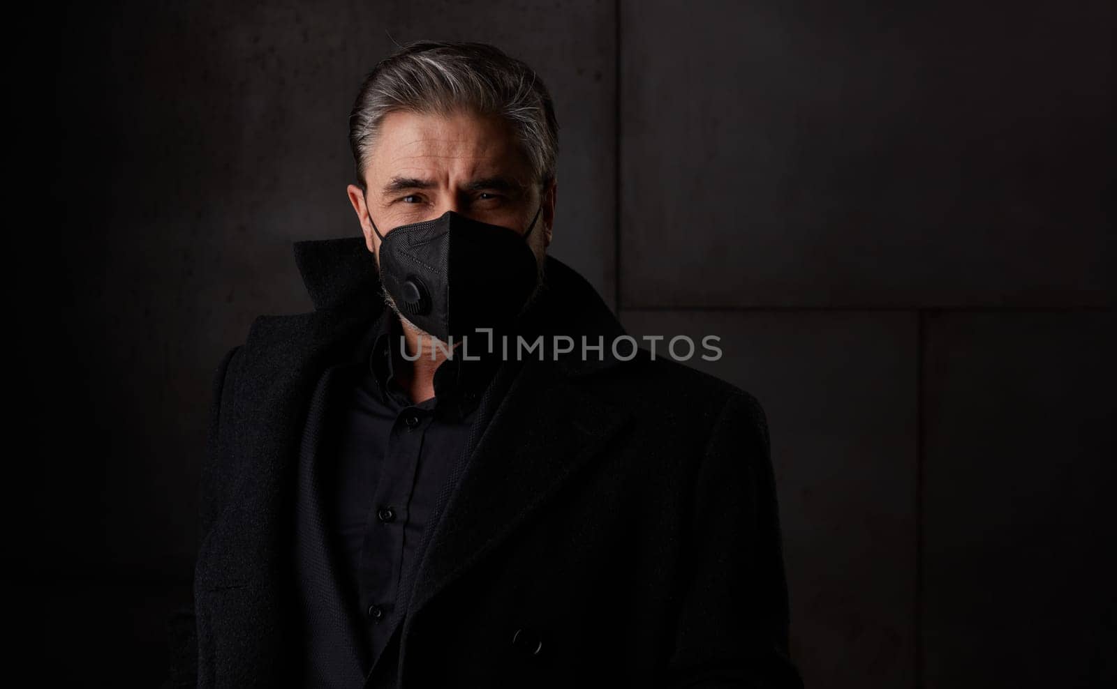 Covid-19 - portrait of older man in 50s with gray hair wearing medical face mask. Dark background copy space.